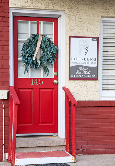 The image shows a red door with a wreath hanging above it, and there s a sign below the wreath with text that includes Loebsberg and a phone number.